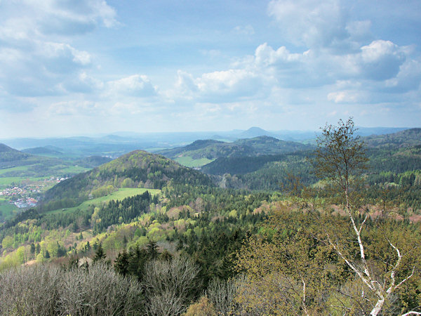 The lookout from the Střední vrch hill to the west. In the foreground on the left side rises the Břidličný vrch with the village Dolní Prysk at its foot, in the middle there is the more distant Jehla with its two peaks and the Kunratický vrch, and at the horizon rises the Růžovský vrch hill.