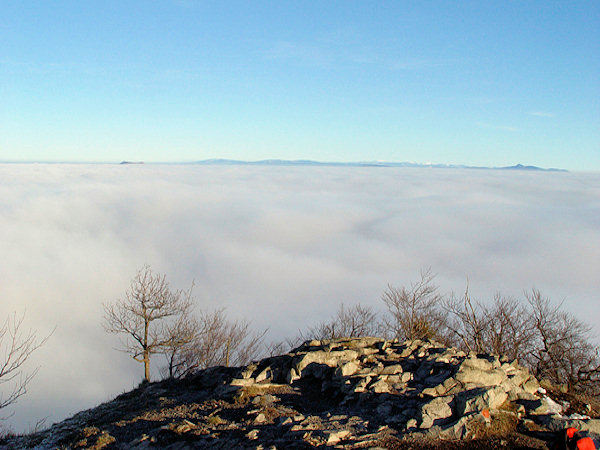 Ein Wolken-Ozean zieht sich bis weit nach Osten hin. Am Horizont links ragt der niedrige Gipfel des Hvozd hervor, von dem sich der bläuliche Streifen des Jizerské hory-Gebirges bis zu den schneebedeckten Gipfeln der Krkonoše weiter hinzieht