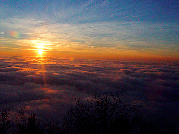The rays of the setting sun illuminate an boundless ocean of clouds.