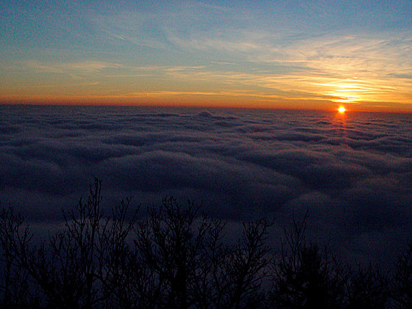 The sun is setting under a layer of clouds.