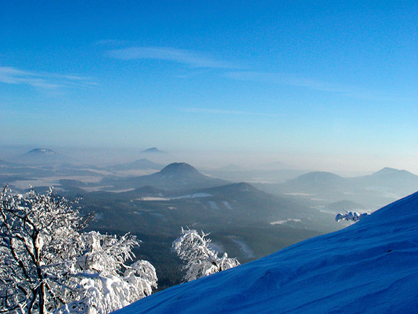 View from the Klíč hill to the Southeast. The most prominent hill in the middle of the picture is the Ortel, before him there is the lower Strážný vrch hill, on the right side the Šišák and the two-peaked top of the hills Tisový vrch and Slavíček. To the left behind of the Ortel hill in the mist there is the Brništský vrch hill, on the horizon rises the Ralsko hill and to the extreme left the Tlustec hill is seen.