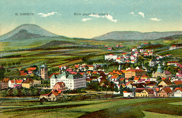 This postcard from 1921 displays the overall view of Česká Kamenice from the foot of the Zámecký vrch hill. In the foreground to the left the building of the school is noticeable, the prominent hill in the background is the Růžovský vrch-hill.