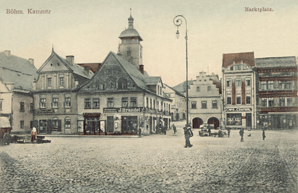 Auf dieser Ansichtskarte von Česká Kamenice (Böhmisch Kamnitz) aus dem Jahre 1906 ist die Südseite des Stadtplatzes mit einem Teil des Hrnčířský trh (Topfmarkt) und der zum Schlosstor führenden Gasse abgebildet.