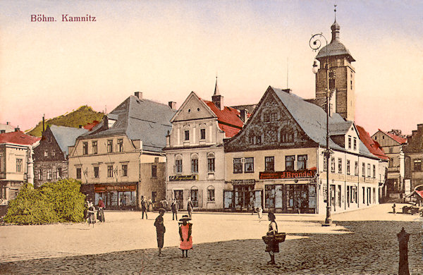 Auf dieser Ansichtskarte von Česká Kamenice aus den Jahren um 1915 sieht man die Südseite des Stadplatzes mit J. Brandels Eisenwarenhandlung an der Ecke. Im Hintergrund ragt der Turm der St. Jakobskirche empor.