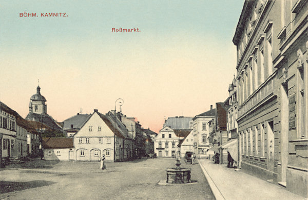 Diese Ansichtskarte von Česká Kamenice (Böhm. Kamnitz) aus dem Jahre 1911 zeigt den Westteil des damaligen Koňský trh (Rossmarkt) mit dem Brunnen. Im Hintergrund der Turm des St. Jakobskirche.