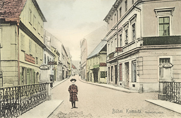 Diese Ansichtskarte zeigt die vom Stadtplatz zur Marienkapelle führende Gasse um 1910. Im Vordergrund ist die Brücke über die Kamenice (Kamnitzbach).