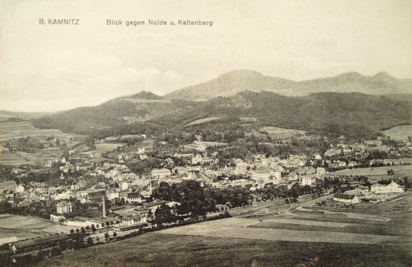 This picture postcard shows the town seen from the foot of Sedlo hill in the direction from the southwest. In the foreground there is the railway station, behind of it the woodland of the Sedlo hill and in the background there is the Studenec hill with the Javorek and Zlatý vrch hills.