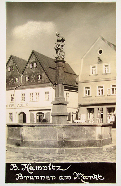 Diese Ansichtskarte zeigt den Springbrunnen mit der Statue der Jungfrau Maria in der Mitte des Stadtplatzes. Das Gebäude des Hotels Adler im Hintergrunde ist später verwahrlost, wurde 1968 abgerissen und neu aufgebaut.