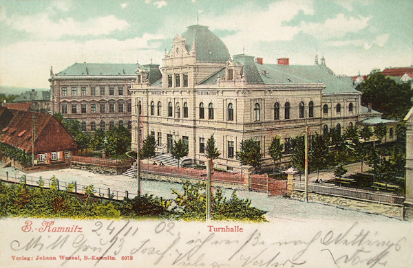Na pohlednici z přelomu 19. a 20. století vidíme tělocvičnu, postavenou v letech 1895-1896, a v pozadí stojící budovu školy z roku 1883. Roubené domky vlevo byly zničené při náletu 8. května 1945.