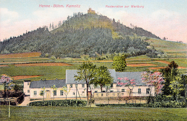 Auf dieser Ansichtskarte von 1913 sieht man die ehemalige, im Februar 1940 vom Feuer vernichtete Gaststätte „Zur Wartburg“ in Huníkov (Henne). Im Hintergrund ist der Zámecký vrch (Schlossberg) mit der Ruine des Kamenický hrad (Schloss Kempnitz).