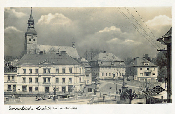 A picture postcard from the 30s of the 20th century showing the northern side of the market-place with the church of St. George in the background. In the foreground there is the old stone bridge which formerly lead across the Chřibská Kamenice-brook.