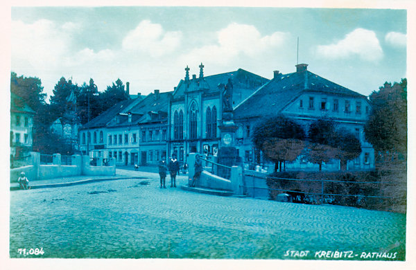 Diese Ansichtskarte zeigt die Häuser an der Ostseite des Marktplatzes, von denen vor allem das pseudogotische ehemalige Rathaus aus dem Jahr 1872 auffällt. Rechts von ihm befindet sich das Geburtshaus Thaddeus Haenkes, das heute als Museum eingerichtet ist.
