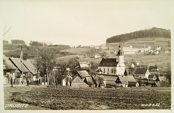 Tato pohlednice zachycuje střed obce s kostelem Nanebevzetí Panny Marie a vrchem Spravedlnost od severozápadu. Budova továrny v pozadí byla po roce 2000 zbořena.