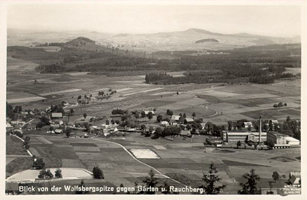 Diese Ansichtskarte zeigt den mittleren Teil der Gemeinde gesehen vom Gipfel des Vlčí hora (Wolfsberg). Aus den Wäldern links ragt der Gipfel des Dymník (Rauchberg) empor.