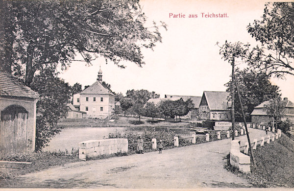 Diese Ansichtskarte aus der Zeit um 1910 zeigt den Damm des Školní rybník (Schulteich) mit der Strasse nach Krásná Lípa (Schönlinde). Von den umgebenden Häusern hat sich bis heute nur die alte Schule (mit dem Türmchen auf dem Dach) erhalten können.