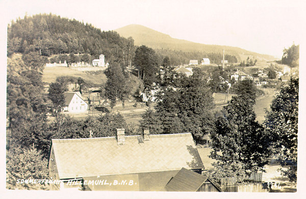 This picture postcard shows the central part of Mlýny with the cemetery. In the background to the right there is the former glass factory „Theresienhütte“.