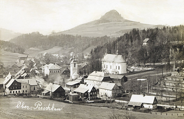 Auf dieser Ansichtskarte sieht man das Ortszentrum mit der vom Friedhof mit dem Glockenturm umgebenen St. Peter u. Paul-Kirche. Im Hintergrunde die charakteristische Silhuette des Střední vrch (Mittenberg).