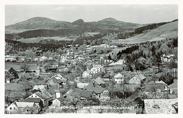 Tato pohlednice zachycuje dolní část Kamenického Šenova. Kopce v pozadí jsou zleva Studenec, Zlatý vrch a Javorek.