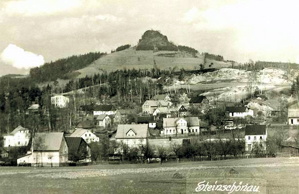 Auf dieser Ansichtskarte ohne Datum sind die Häuser des niederen Teiles von Kamenický Šenov (Steinschönau) am Fusse eines Hügels mit Sandsteinbrüchen. Im Hintergrude ragt der charakteristische Felsen des Střední vrch (Mittenberg) in die Höhe.