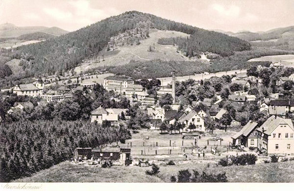 Diese Ansichtskarte zeigt den zentralen Teil der Stadt mit der Kirche und dem auffallenden Schulgebäude. Im Hintergrund ist der Šenovský vrch (Steinschönauer Berg).