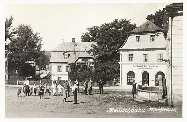 Auf dieser Ansichtskarte wird ein Teil des Stadtplatzes mit dem Gebäude der „Kreditanstalt der Deutschen“, und vor ihr der an die Seitenwand des Stadtmuseums angebaute steinerne Brunnen abgebildet. Beide Häuser wurden später abgerissen und bis heute hat sich nur das im Hintergrunde stehende Haus No. 51 und der Brunnen erhalten.