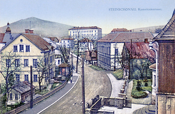 Diese Ansichtskarte von 1913 zeigt die Hauptstrasse im Blick von Česká Kamenice (Böhmisch Kamnitz). Im Hintergrunde steht das grossartige Schulgebäude und am Horizont hinter ihm ragt der Šenovský vrch (Schönauer Berg) hervor.