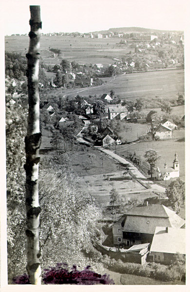 Diese Ansichtskarte zeigt das von den Felsen am Freibad gesehene untere Ende von Kamenický Šenov (Steinschönau). Im Vordergrund steht die ehemalige Mühle und an der Strasse unweit von ihr die heute schon abgerissene Dreifaltigkeitskapelle.