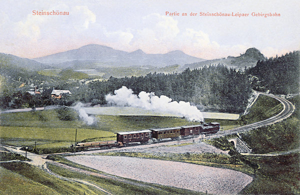 Die Ansichtskarte aus dem Jahre 1910 zeigt die heute schon stillgelegte Bergeisenbahnstrecke von Kamenický Šenov (Steinschönau) nach Česká Lípa (Böhmisch Leipa) ein Stück hinter dem unteren Bahnhof. Rechts erhebt sich der charakteristische Gipfel des Střední vrch (Mittenberg) und hinter ihm am Horizont die Berge der Umgebung des Studenec (Kaltenberg).
