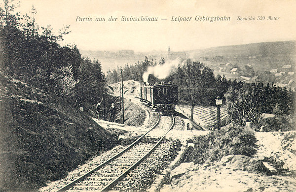 Auf dieser Ansichtskarte aus dem Jahre 1906 sieht man einen aus Česká Lípa (Böhmisch Leipa) kommenden Zug im Bogen der Strecke am Hange des Šenovský vrch (Steinschönauer Berg). Im Hintergrund sieht man Kamenický Šenov (Steinschönau) und seine Kirche.