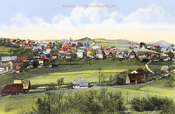 This picture postcard shows the village Prácheň as seen from the slope of the Vyhlídka-hill. On the right side there is the road to Kamenický Šenov and behind the church you see the rather small hill of the Panská skála rock.