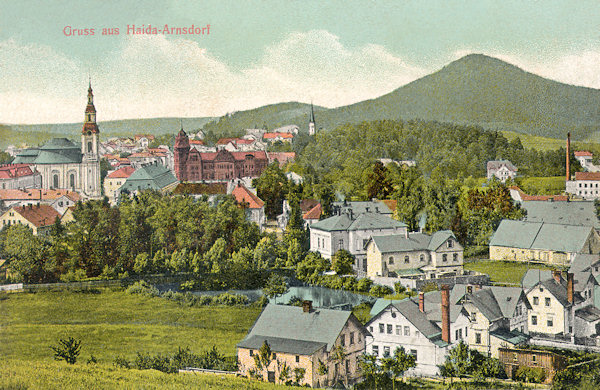 Diese Ansichtskarte vom Anfange des 20. Jahrhundert zeigt das Stadtzentrum mit der Kirche Mariä Himmelfahrt und dem monumentalen Gebäude der Sparkasse. Die Häuser im Vordergrund gehören bereits zu Arnultovice (Arnsdorf), das allmählich mit Nový Bor zusammenwuchs. Im Hintergrund links ist der Chotovický vrch (Kottowitzerberg).