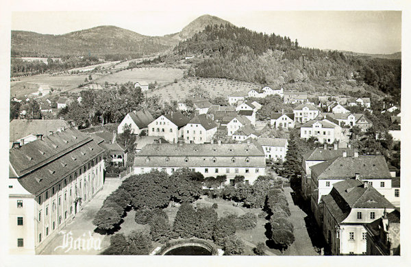 Auf dieser Ansichtskarte aus der Zeit zwischen den beiden Weltkriegen sieht man den kleinen Park im Nordteil des Stadtplatzes. Das grosse Haus links ist seit 1821 Sitz der städtischen Behörden, im Hause rechts im Vordergrund befindet sich das Glasmuseum. Über der Stadt erhebt sich der niedrige Borský vrch und am Horizont de spitzige Gipfel des Klíč-Berges (Kleis).