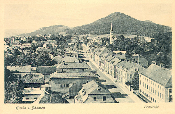 Diese Ansichtskarte aus den 20er Jahren des 20. Jahrhunderts zeigt die ehemalige Poststrasse, die vom Stadtplatz nach Česká Lípa (Böhm. Leipa) führt, vom Turm der Kirche Mariä Himmelfahrt aus gesehen. Im Hintergrund sieht man den Turm der evangelischen Kirche, die 1982 durch Brand zerstört wurde, am Horizont erhebt sich der Chotovický vrch (Kottowitzer Berg).