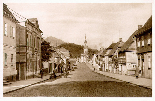 Diese Ansichtskarte dokumentiert die ursprüngliche Bebauung der Poststrasse (heute T. G. Masaryk-Strasse), die vom Stadtplatz in Richtung auf Česká Lípa (Böhm.-Leipa) hinausführt. Die Häuser an der rechten Strassenseite sind in den 70er Jahren des 20. Jahrhunderts abgerissen worden und wurden durch Grossplattenhäuser ersetzt. Im Hintergrund sieht man die am Stadtplatz stehende Mariä Himmelfahrt-Kirche.