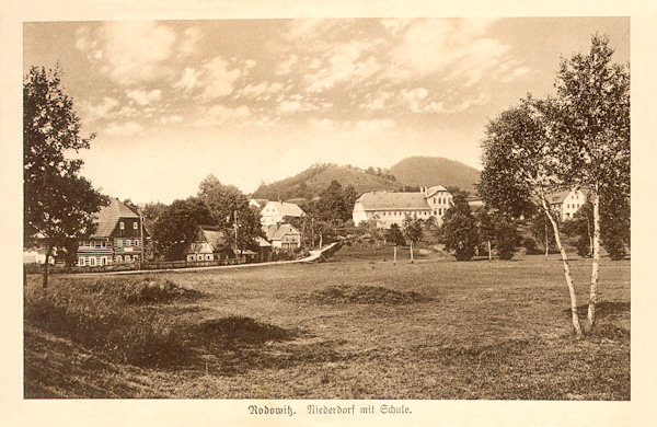 On this picture postcard from the first half of the 20s of the 20th century we see the lower part of the village with the monumental building of the former seignorial farmyard, in which since 1881 the primary school was located. Behind of the village there is the Pomahačův vrch hill and behind it the Strážný hill.