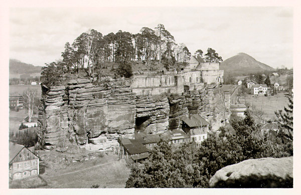 This postcard shows the view of rock tower of the Poustevnický kámen (Hermite-rock) from the edge of the rock massif rising in the southern neighbourhood above the valley of the brook Dobranovský potok.