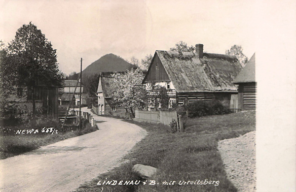 Auf dieser Ansichtskarte aus den 20er Jahren des 20. Jahrhunderts sieht man einige Häuser an der Strasse von Kunratice. Das Haus im Vordergrud steht heute nicht mehr, das Fachwerkhaus hinter ihm wurde in der letzten Zeit rekonstruiert. Hinter dem Baum links sieht man einen Teil der damaligen Gaststätte „Zu den drei Brücken.