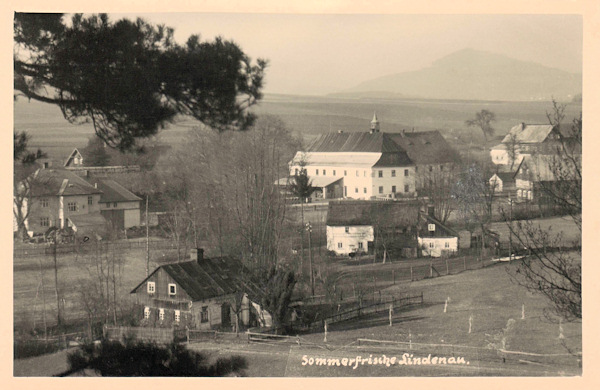 Na této pohlednici vidíme dolní část obce s výraznou budovou nejstarší lindavské brusírny zrcadel, kterou v letech 1918-1945 využívala firma Eckert-Heidrich k výrobě umělého kamene a cementového zboží. Po 2. světové válce byla budova zbořena a dnes zde stojí nový rodinný domek.