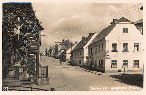 Tato pohlednice zachycuje střední část nynější Komenského ulice, která dnes vypadá úplně jinak. Roubený dům s krásně zdobeným křížem tu dnes již nenajdeme a zbořeny byly i dva nejbližší domy na pravé straně ulice.