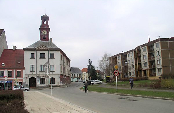 Na srovnávacím snímku ze současnosti vidíme pouze radnici s věží poněkud nižší než na dobové pohlednici a fasádou již bez charakteristických štukatur.