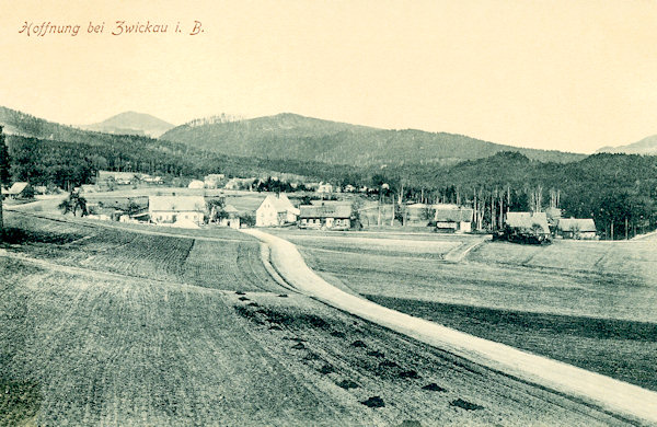 Auf dieser Ansichtskarte sehen wir Naděje (Hoffnung) von der Strasse aus Trávník (Glasert) aus. Im Hintergrund hinter der Ansiedlung ist der Kamenný vrch (Steinberg) und links von ihm am Horizont der Luž-Berg (Lausche).