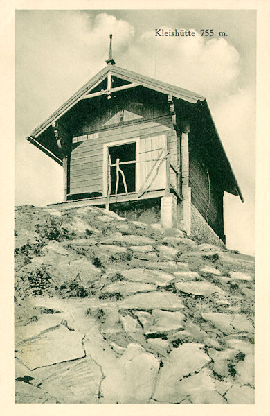Diese Ansichtskarte aus den Jahren um 1930 zeigt die letzte aus der Reihe der touristischen Schutzhütten auf dem Gipfel des Klíč (Kleis). Das Blockhaus wurde 1910 errichtet und bestand bis 1938, als es auf Befehl der militärischen Behörden der damaligen Tschechoslowakischen Republik abgerissen werden musste.