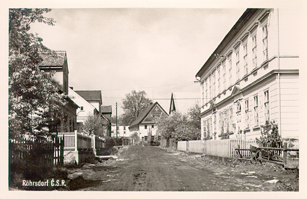 Auf dieser Ansichtskarte aus den Jahren zwischen beiden Weltkriegen sieht man die Hauptstrasse im Ortszentrum. Das auffalende Gebäude rechts, in dem heute das Postamt und die Gemeindeverwaltung untergebracht sind, verlor im Laufe der Umbauten in der 2. Hälfte des 20. Jh. sein monumentales Aussehen.