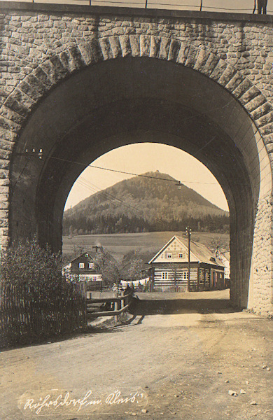 Diese Ansichtskarte zeigt einige Häuser des Oberortes und den Klíč-Berg im Hintergrund im Blick durch die Öffnung der Eisenbahnbrücke.