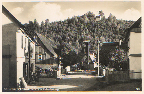 Diese Ansichtskarte aus den 30er Jahren des 20. Jahrhunderts zeigt die Kapelle auf dem Kalvarienberg im Blick von der Hauptstrasse an der Abzweigung nach Heřmanice (Hermsdorf). Vor Richters Gasthaus stand damals der von der Eisengiesserei Neuwinger in Mařenice (Mergtal) hergestellte Feuerwehrturm, im Vordergrund links ist das Haus des Kolonial- und Gemischtwarenhändlers Anton Engel No. 161.