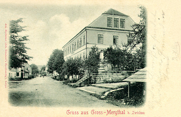Diese Ansichtskarte von 1901 zeigt die Hauptstrasse in der Ortsmitte mit dem Monumentalgebäude der Schule und dem ehemaligen Gefallenendenkmal.