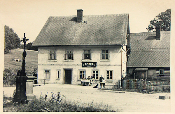 Diese Ansichtskarte zeigt das ehemalige Winklersche Geschäft an der Abzweigung zum Forsthaus in der 2. Hälfte der 40er Jahre des 20. Jahrhundert, als es der Nordböhmischen Konsumgenossenschaft SKD gehörte. Das Kreuz im Vordergrund wurde später vernichtet und an seiner Stelle blieb nur der Sockel, auf dem man 2004 eine neues schmiedeeisernes Kreuz aufstellte.