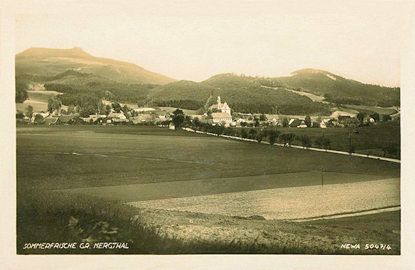 Diese Ansichtskarte bildet das Zentrum von Mařenice (Mergtal) mit der Kirche der hl. Maria Magdalena von Westen gesehen ab. Die Strasse im Vordergrund führt nach Cvikov (Zwickau), hinter der Gemeinde rechts sieht man den Zámecký vrch (Schlossberg) und links im Hintergrund den Hochwald (Hvozd) an der Staatsgrenze.