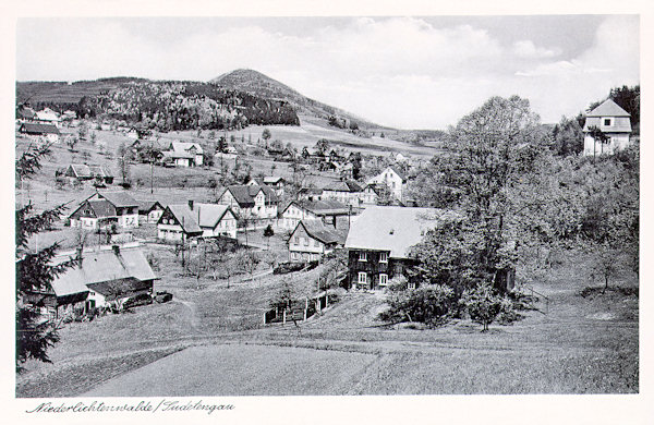 Tato pohlednice ze 30. let 20. století zachycuje domky v dolní části obce pod bývalou školou. V pozadí je hora Luž.