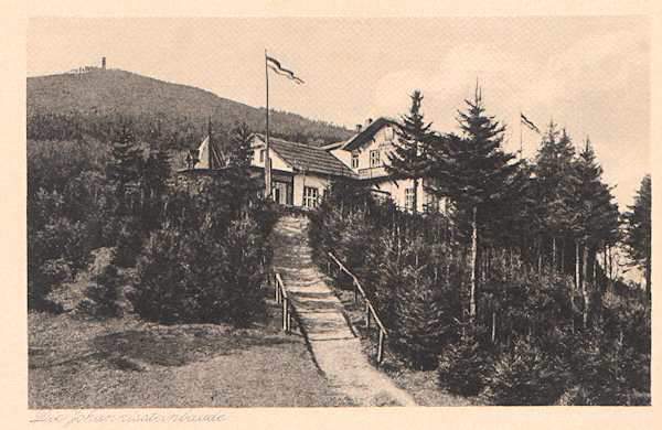 This picture postcard shows the peak of the Janské kameny - Johannissteine with the restaurant which in the course of the years was overgrown by wood, at about 1920 when a part of the timbered veranda had been replaced by a brickwall construction. The Hvozd - Hochwald hill was artificially painted into the background as actually it is situated on the other side of the hill.